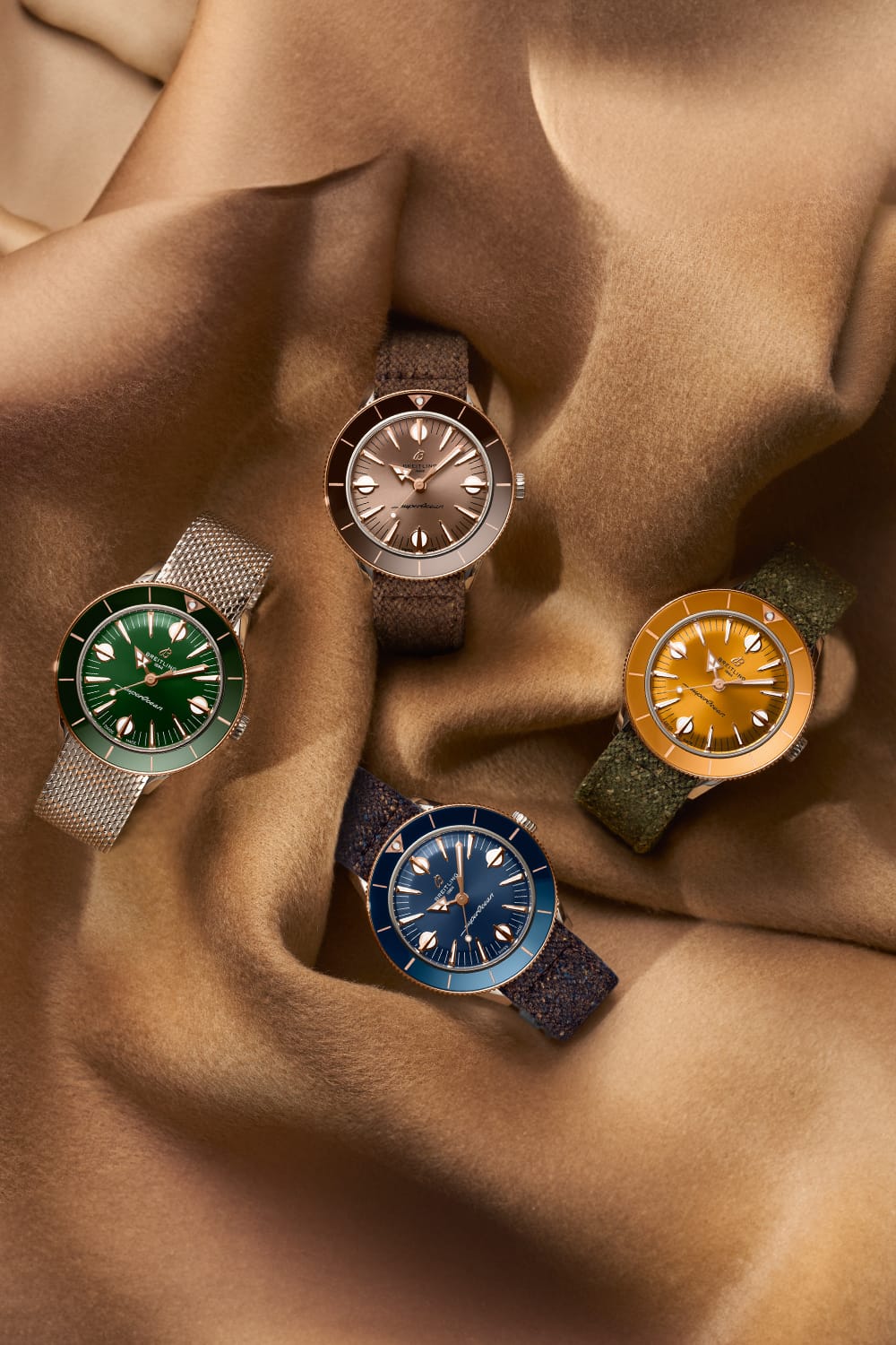 Four different colored Superocean Heritage watches lie on a brown cloth.