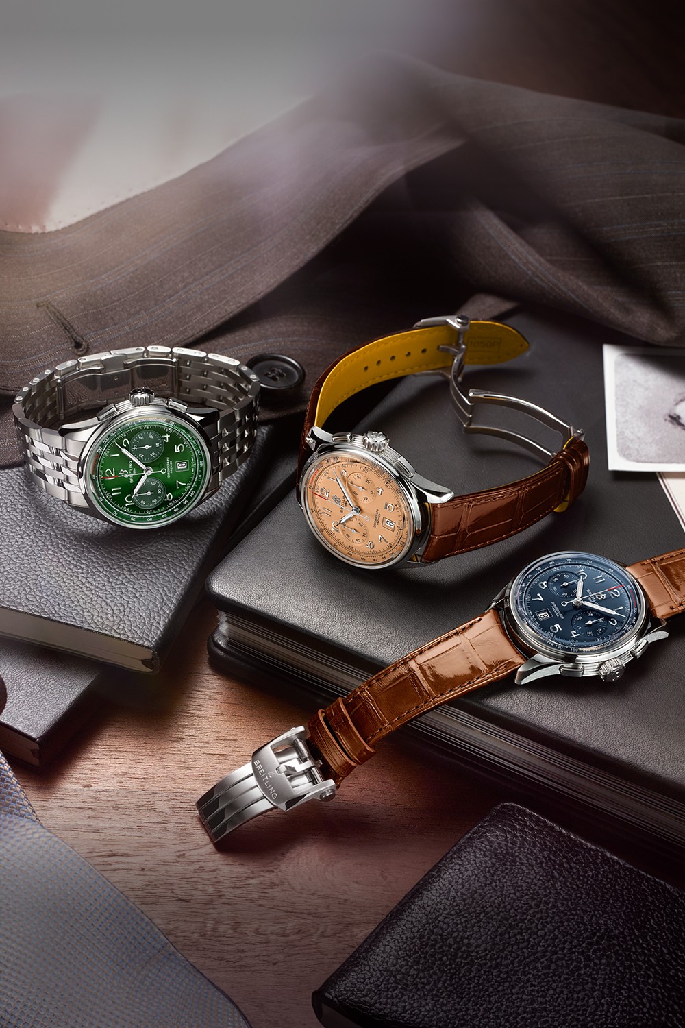 Three Premier watches with elegant bracelets lie on black notebooks on a brown table.