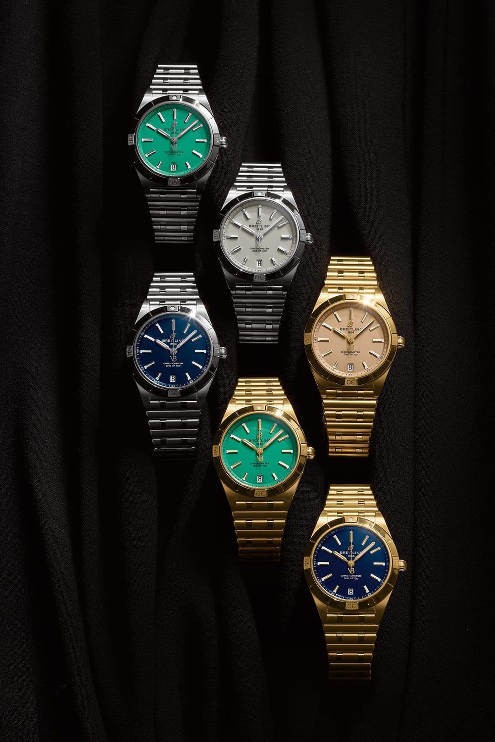 Three silver and three gold Chronomat watches with different-colored dials against a black background.