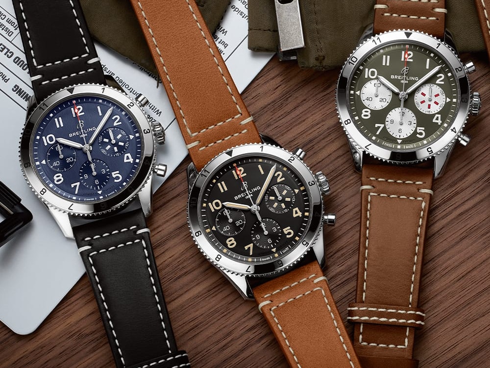 Three Classic AVI with different colored, dark leather straps on a dark brown table.