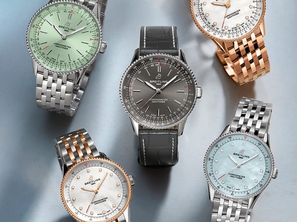 Five Navitimer watches with different-colored dials lie on a blue cloth.