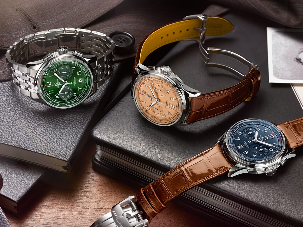 Three Premier watches with elegant bracelets lie on black notebooks on a brown table.