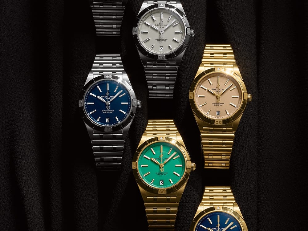 Three silver and three gold Chronomat watches with different-colored dials against a black background.
