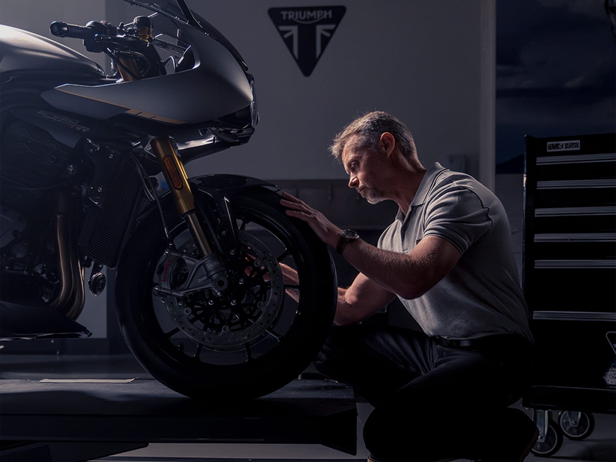 Man with Breitling watch in focus kneels in front of Triumph motorcycle