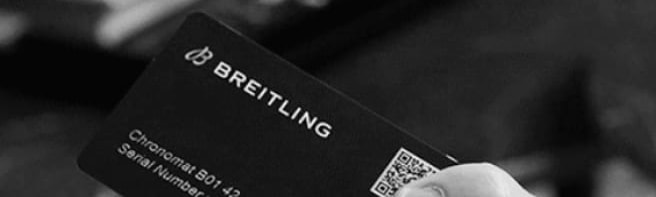 A male hand holds a Breitling warranty card with the inscription Chronomat B01 42.