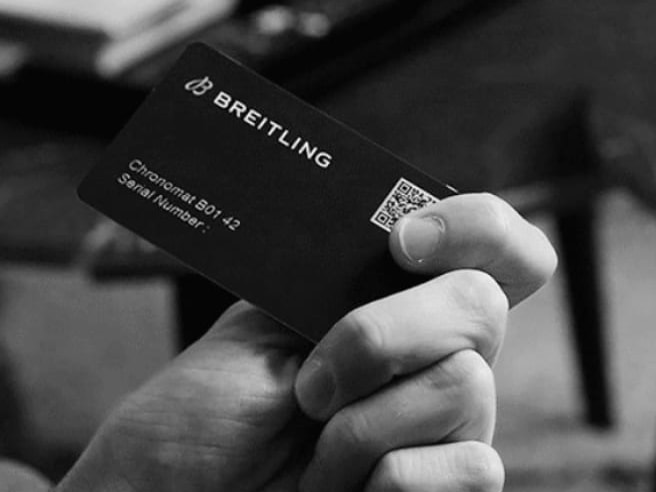 A male hand holds a Breitling warranty card with the inscription Chronomat B01 42.