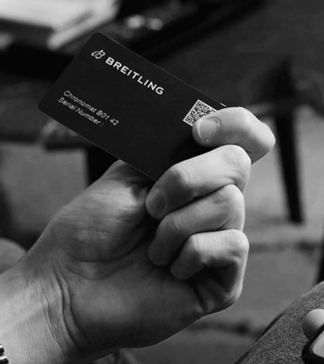 A male hand holds a Breitling warranty card with the inscription Chronomat B01 42.