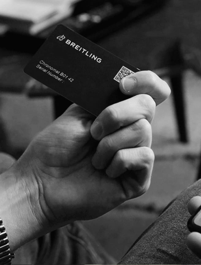 A male hand holds a Breitling warranty card with the inscription Chronomat B01 42.
