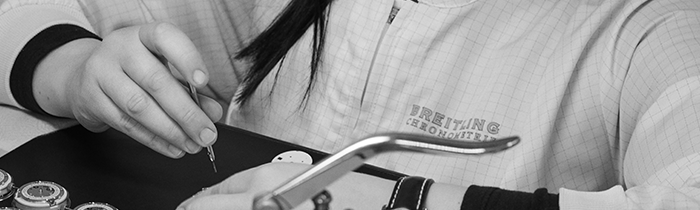 A man has a watchmaker's loupe clamped in his eye and is working on a Breitling watch.