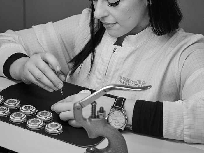 A man has a watchmaker's loupe clamped in his eye and is working on a Breitling watch.