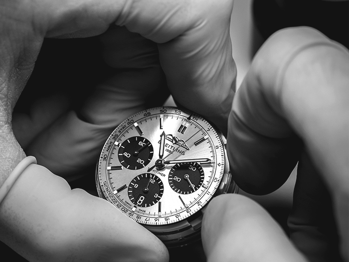 A man has a watchmaker's loupe clamped in his eye and is working on a Breitling watch.