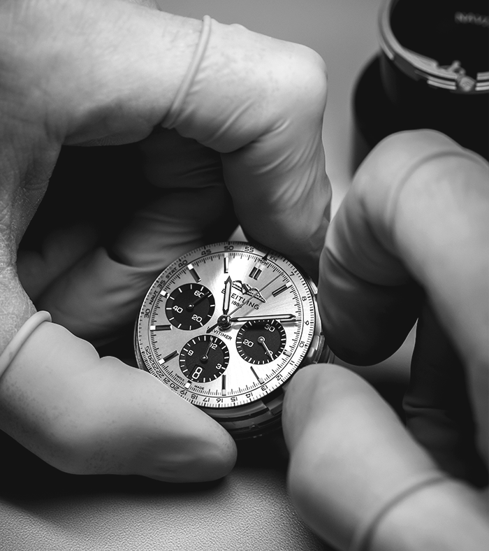 A man has a watchmaker's loupe clamped in his eye and is working on a Breitling watch.