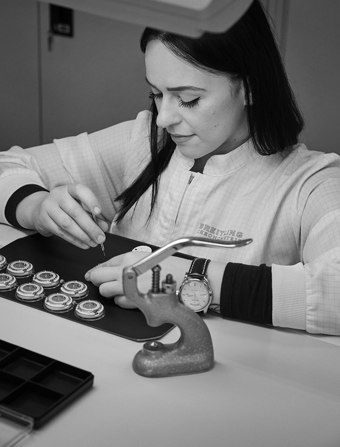 A man has a watchmaker's loupe clamped in his eye and is working on a Breitling watch.