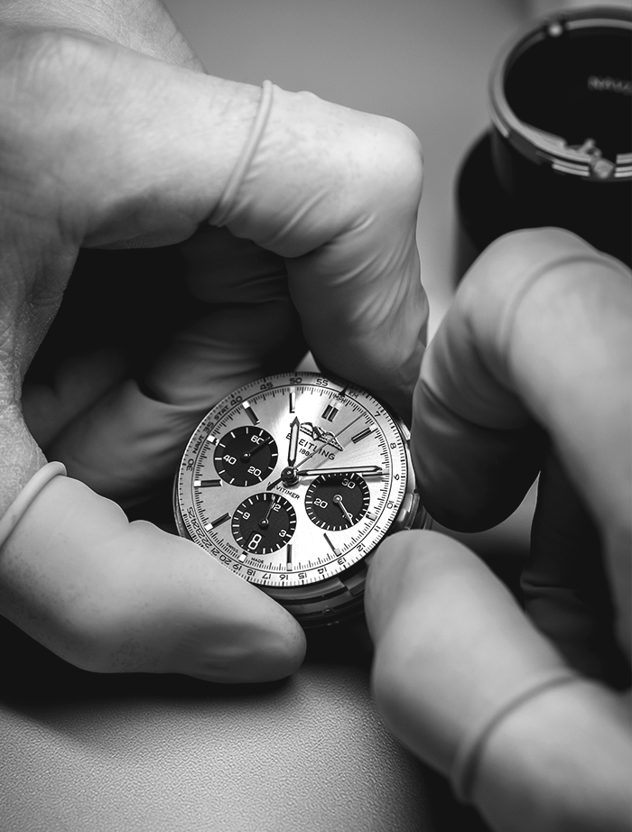 A man has a watchmaker's loupe clamped in his eye and is working on a Breitling watch.